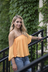 Stunning young blonde fashion model poses in orange blouse with bare shoulders and blue jeans on...