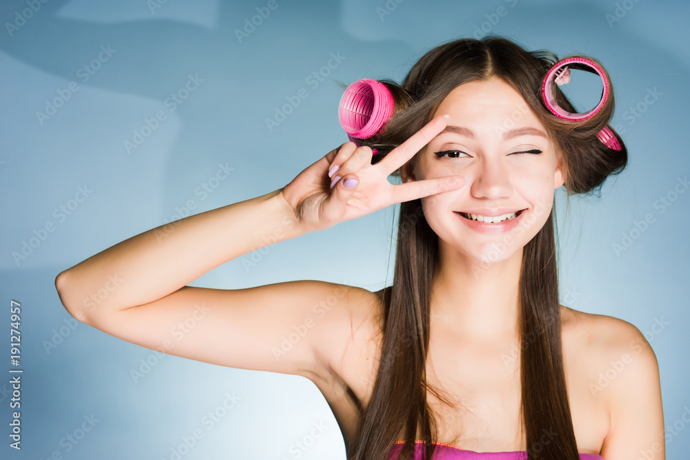 Poster happy smiling girl showing two fingers on head of curler