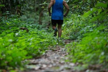Athletic runner running on tropical forest trail, dramatic tone