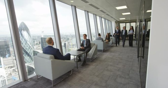 4K Serious business management team talking as they walk through London office. View from window shows some of London's most iconic buildings. Slow motion.