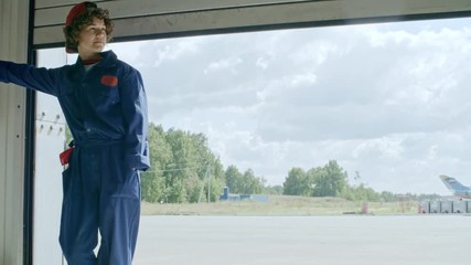 Young female aircraft mechanic pushing the button and opening folding door of aircraft hangar - Powered by Adobe