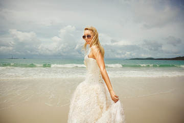 young woman in wedding dress goes over sea turning back. bride on the beach.