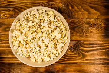 Ceramic plate with popcorn on wooden table. Top view