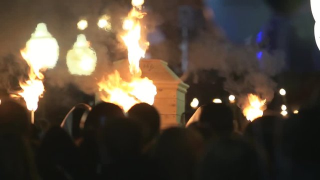 Crowd of people with torches carry a coffin at night