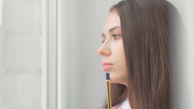 Thoughtful attractive young woman looking outside through a window