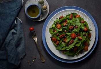 Spinach salad with roasted pecans,pomegranate seeds,cherry tomatoes and dry cranberries on rustic background