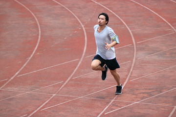 Young athlete Asian man running on racetrack in stadium. Healthy active lifestyle concept.