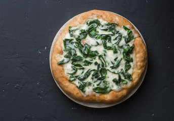 White spinach mozzarella pizza on a dark background, top view