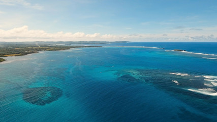 Coastline of the tropical island Siargao with the mountains and the rainforest on a background of ocean with big waves. Aerial view: sea and the tropical island with rocks, beach and waves. Seascape
