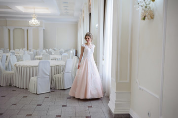 A beautiful woman in a pink wedding dress in a big festive hall