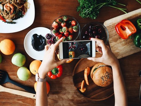 Woman hand holding smart phone for taking a photo food on table.