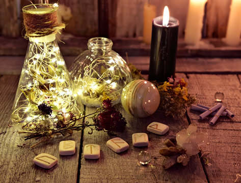 Magic bottles with lights, runes and black candle on witch table. Occult, esoteric, divination and wicca concept. Halloween background with vintage objects 