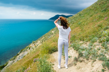 Young woman worth of grief and looks at sea, back view. Hand above the head.