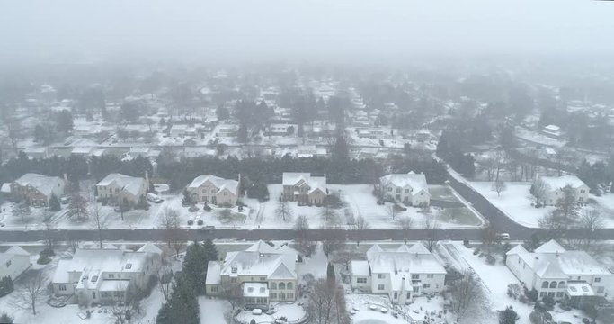 Aerial view of dense rows of Pennsylvania houses standing under heavy snowfall with a plowed street cutting across. Thick fog swallows the distance in a bleak hushed Pennsylvania winter scene.