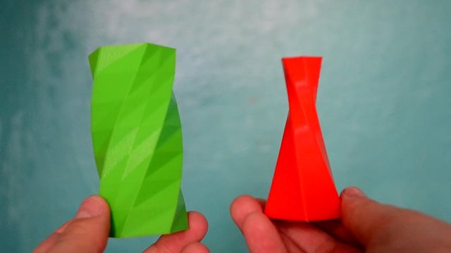 Person holds on hands and view green and red objects created on 3d printer. POV, point of view, mtb. Fused deposition modeling, FDM. Progressive modern 3D printing additive technology. 4ht revolution.