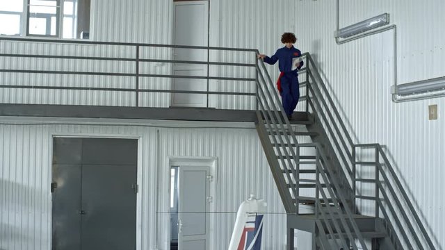Female aircraft maintenance supervisor entering hangar and going downstairs to light jet airplane