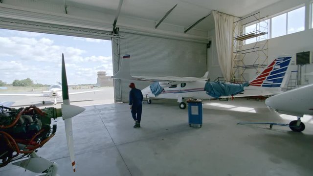 Tilt up high angle of female pilot walking out of hangar and getting into light jet airplane