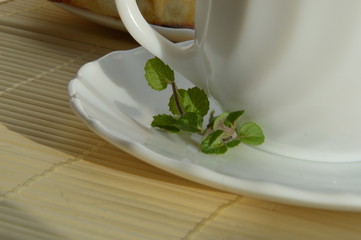 black tea with mint in white mug on white plate on straw stand