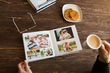 the Hand senior woman holding a family photo album against the background of the a wooden table. - obrazy, fototapety, plakaty