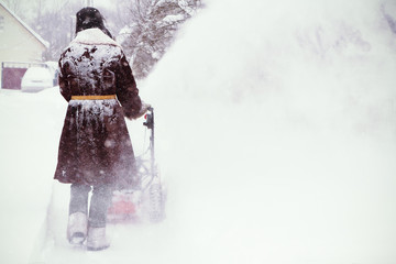 Man in sheepskin coat clears snow with snow blower