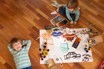 Happy cheerful children drawing with brush in paper using a lot of painting tools.   Top view.