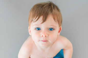 Portrait of a blonde baby boy with blue eyes on a gray background