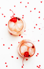 Pink alcoholic cocktail for Valentines day, two glasses, white background with sweet hearts, top view