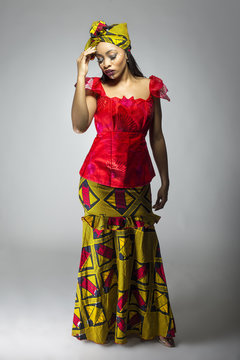 Black Female Showing African Pride By Wearing A Traditional Nigerian Dress And Head Scarf With Tribal Face Markings Or Cosmetic Makeup.  The Costume Is Red And Yellow And Shows Cultural Fashion.