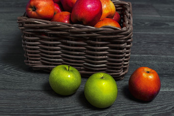 Basket with red and green apples stands on a gray wooden background.
