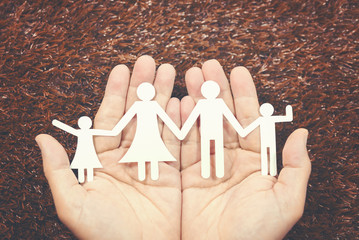 Paper family on hands and green grass background,family and care concept.