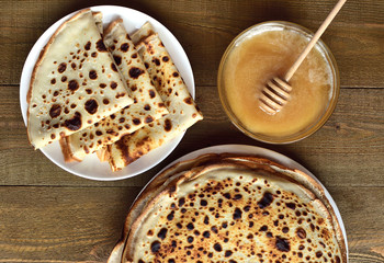 top view of a plate with fresh homemade pancakes, a bowl of honey and a hot stack of pancakes on a brown wooden table
