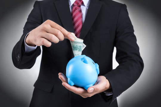 Male hand putting bank dollar into a piggy bank.