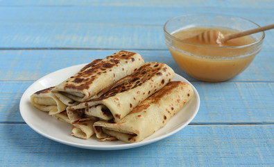Delicious home made pancakes with bowl of honey on a blue retro wooden background. Traditional crepes for pancake week or Shrovetide (maslenitsa holidays) on blue retro background