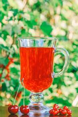 glass of juice from cherry berries and red currants and fresh berries on green natural background