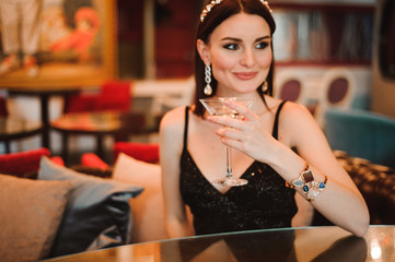 A beautiful girl drinks martini in the hotel lobby and is waiting for her young boyfriend