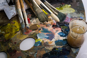 set of different brushes and oil paints to paint scattered on a dark wooden table top view