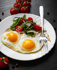 Breakfast. Fresh salad and two fried eggs on dark wooden background