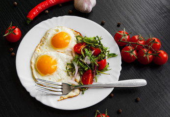 Breakfast. Fresh salad and two fried eggs on dark wooden background