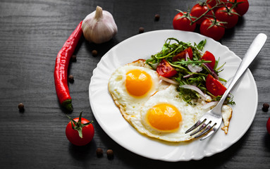 Breakfast. Fresh salad and two fried eggs on dark wooden background
