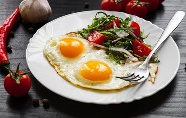 Breakfast. Fresh salad and two fried eggs on dark wooden background