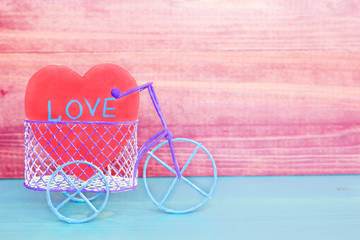 Toy bicycle and paper heart on the wooden table, love concept.