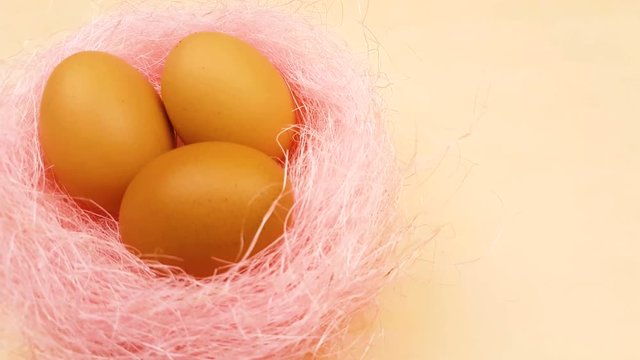 Easter yellow eggs in pastel pink nest on yellow background. Close up in minimalism style.