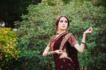 Beautiful young caucasian woman in traditional indian clothing sari with bridal makeup and jewelry and henna tattoo on hands