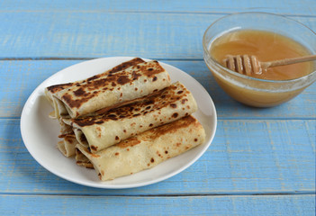 Pancakes and honey Maslenitsa. A pile of pancakes, honey, for the celebration of the carnival. Thin pancakes for breakfast. Pancakes with honey on a blue retro wooden background.
