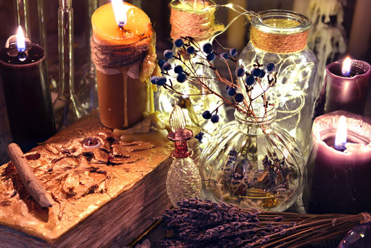 Evil book with black candles, glass bottles, and herbs on witch table. Occult, esoteric, divination and wicca concept. Halloween background with vintage objects 