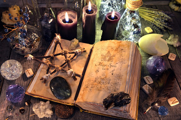 Old witch book with pentagram, black candles, crystals and ritual objects. Occult, esoteric, divination and wicca concept. No foreign text, all symbols on pages are fantasy, imaginary ones  - obrazy, fototapety, plakaty
