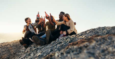 Friends sitting on mountain top and toasting beers