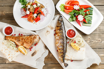 grilled mackerel and sea bass. Salad of fresh vegetables. Serving on a wooden Board on a rustic table. Barbecue restaurant menu, a series of photos of different meats anf fish