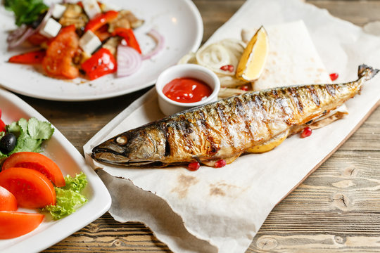 grilled mackerel and a salad of fresh vegetables. Serving on a wooden Board on a rustic table. Barbecue restaurant menu, a series of photos of different meats anf fish