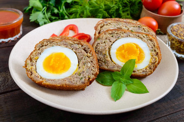 Meat cutlet with boiled egg, pieces on a ceramic plate on a dark wooden background. Mini meat rolls. Scottish cutlet.